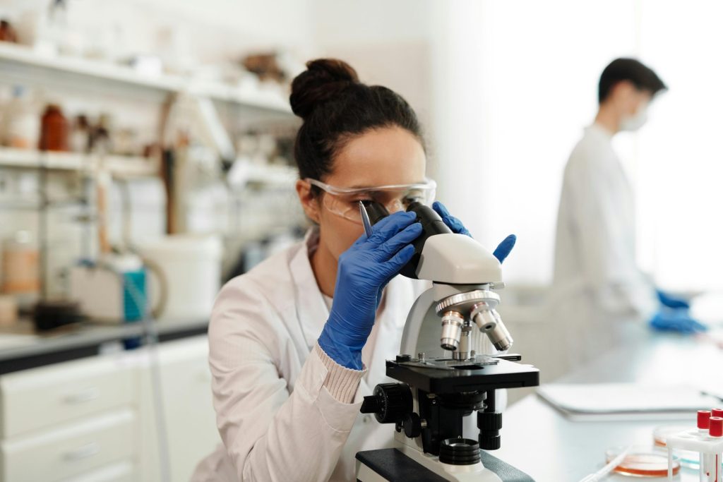Eine Wissenschaftlerin in Schutzkleidung untersucht in einem Labor Proben unter einem Mikroskop.